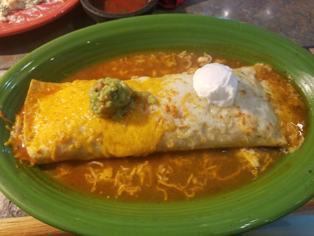 A mexican burrito with enchilada sauce, sour cream and guacamole.