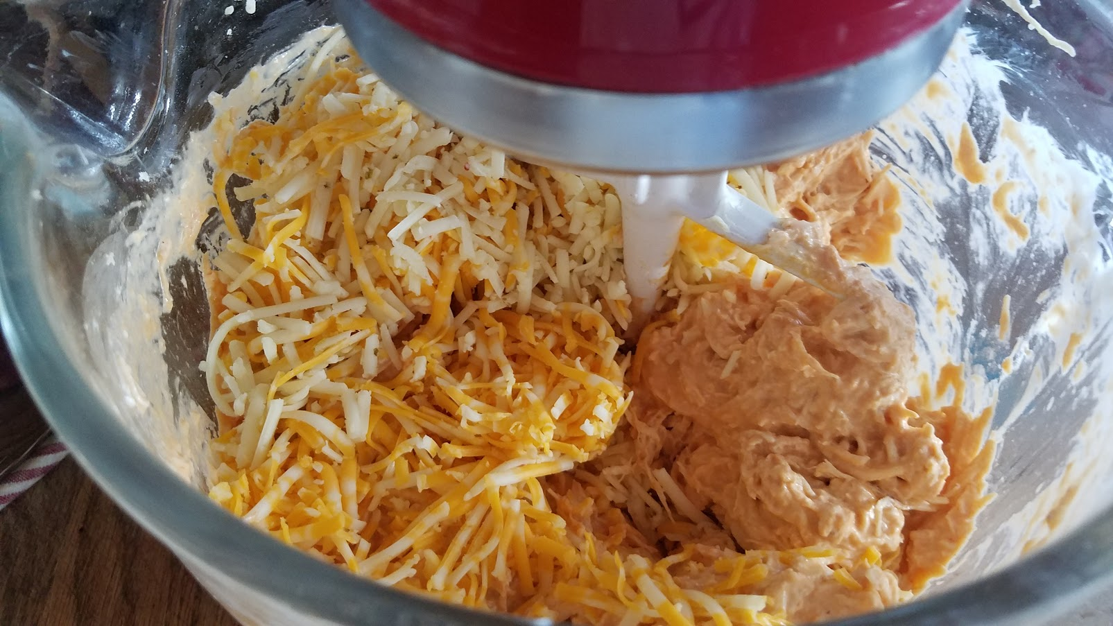 A glass bowl with shredded creamy cream cheese, buffalo sauce chicken, and cheese.