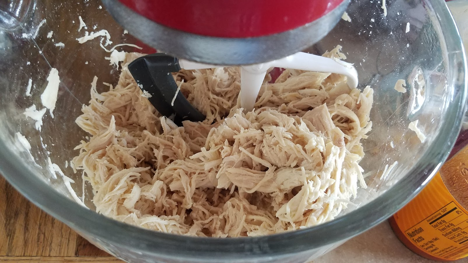 A bowl with a shredded chicken in it with a Kitchenaide paddle attachment 