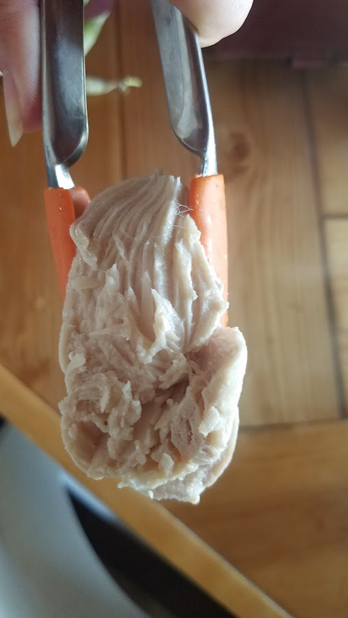 Tongs holding a cooked piece of boiled chicken