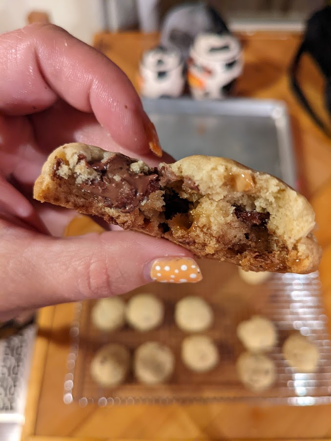A hand holding a half of a chocolate chip cookies with melting chocolate chips.
