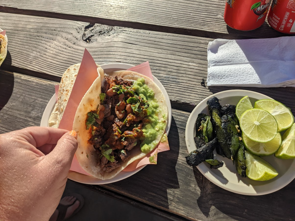 A hand holding open a carne asada taco with limes and fried jalapenos on the side from tacos El Yaqui, rosarito mexico.